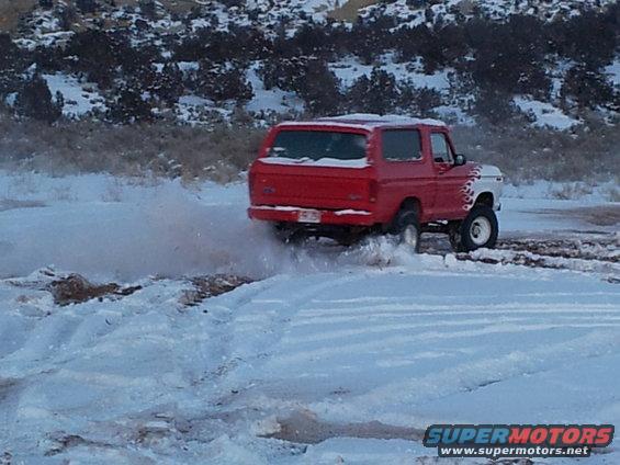 Red 1979 Ford Bronco kicking up snow while driving off-road