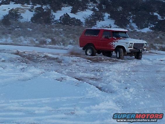 Red and white 1978 Ford Bronco with flame decals driving in snow, front-right quarter view