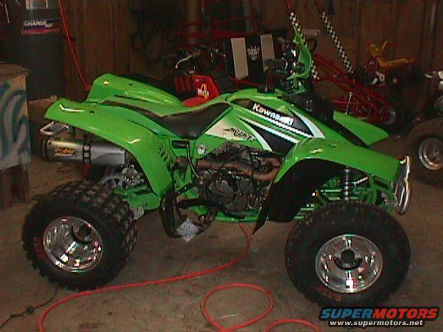 Green Kawasaki ATV parked in a garage with other vehicles in the background