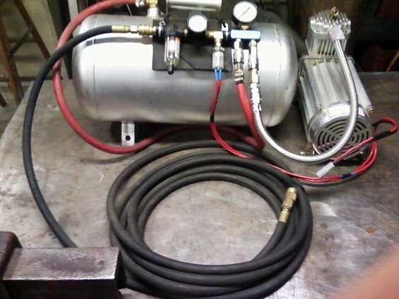 Air compressor tank with gauges, regulator, and hoses connected to a small compressor unit