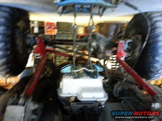 Engine and suspension components under a vehicle, possibly a 1978 Ford Bronco