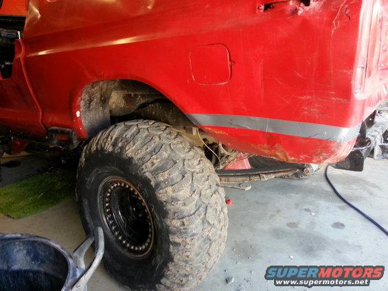 Red pickup truck rear quarter panel with large off-road tire. Appears to be a 1970s model