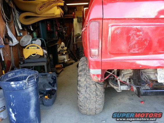 Rear of red pickup truck with large tires, parked in a garage with tools and equipment