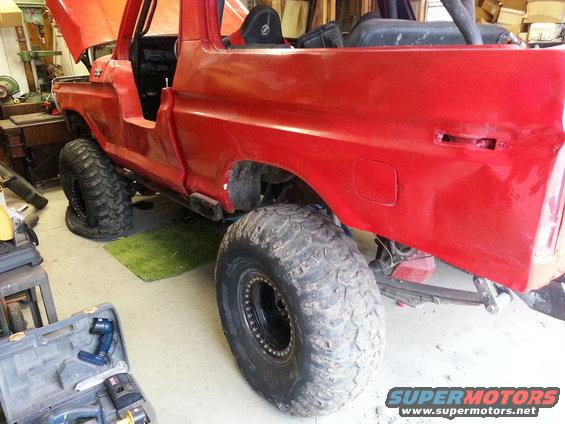 Red 1978 Ford Bronco with large off-road tires, hood open, in a garage