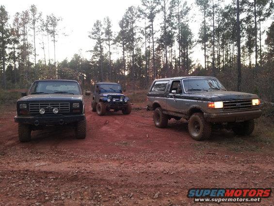 Ford Bronco, Ford pickup, and Jeep parked on a dirt road in a wooded area