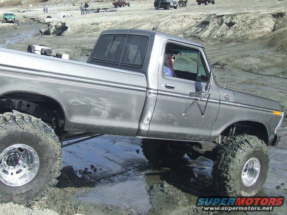Lifted gray pickup truck with large tires in a muddy area. A person is driving