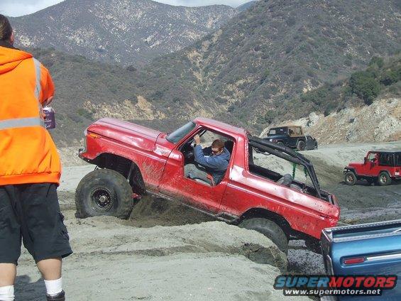 Red 1978 Ford Bronco navigating sandy terrain with a roll cage