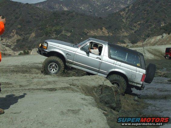 Silver SUV with off-road tires navigating a muddy incline, driver visible