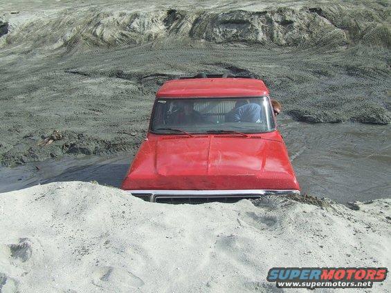 Red truck stuck in mud. The front end is submerged in water and sand