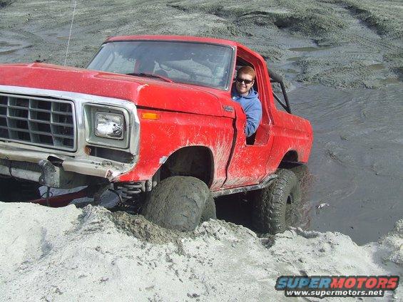 Red 1978 Ford Bronco stuck in mud with driver smiling