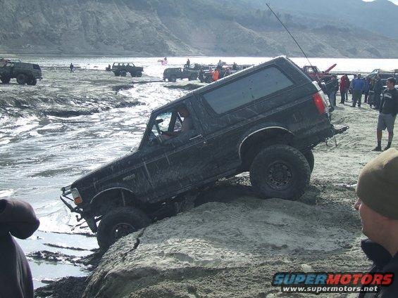 Black Ford Bronco attempting rocky incline with other vehicles and people in background