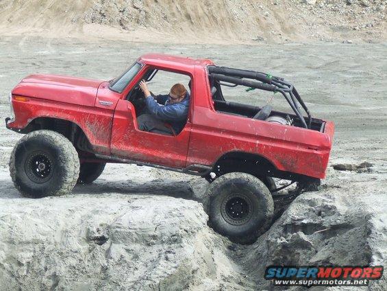 Red 1978 Ford Bronco with large tires navigating rocky terrain