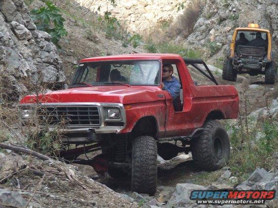 Red 1978 Ford Bronco off-roading on a rocky trail, front 3/4 view