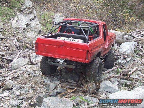Red 1978 Ford Bronco with roll cage on rocky terrain