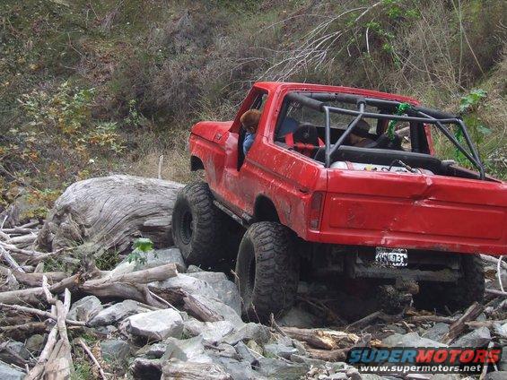 Red 1978 Ford Bronco with roll cage, lifted suspension, and large tires navigating a rocky trail