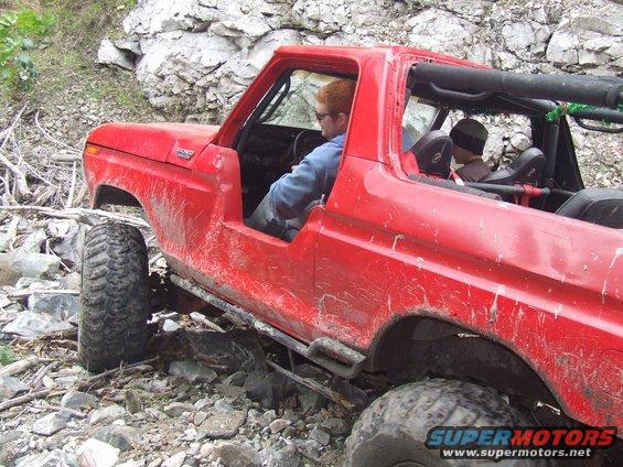 Red 1978 Ford Bronco off-roading on a rocky trail, driver visible