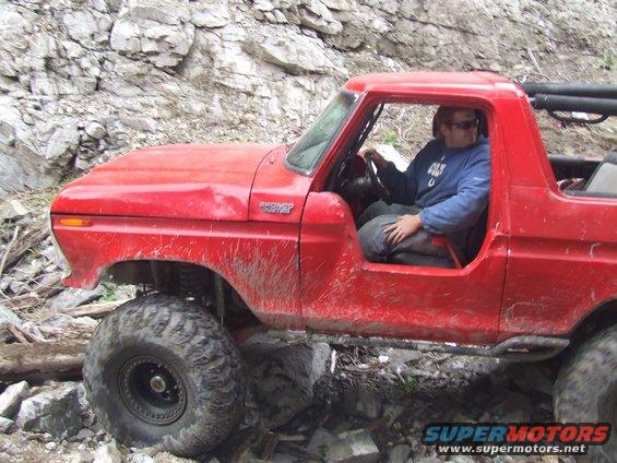 Red 1978 Ford Bronco off-roading over rocks with driver inside