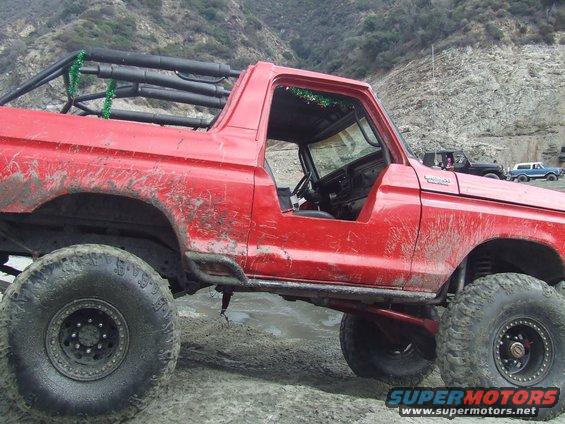 Mud-covered red 1978 Ford Bronco with roll cage and off-road tires parked on dirt