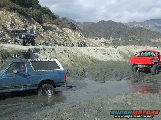 Blue SUV stuck in mud with a red truck nearby