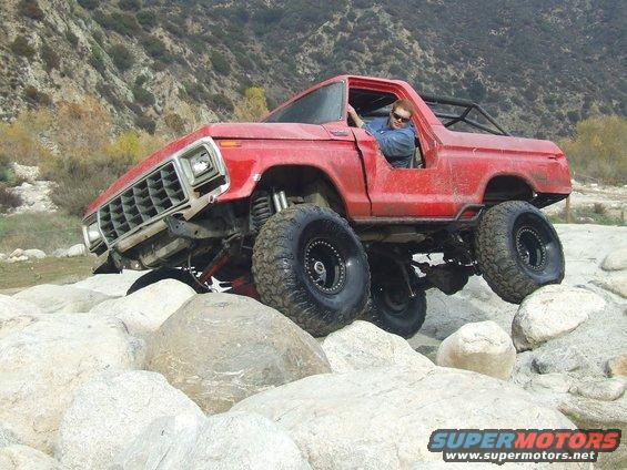 Red 1978 Ford Bronco off-roading over large rocks