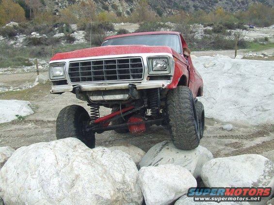 Red 1979 Ford F-Series truck with lifted suspension navigating rocks