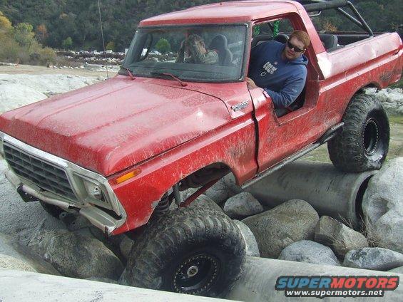 Red 1978 Ford Bronco off-roading over rocks and concrete pipes