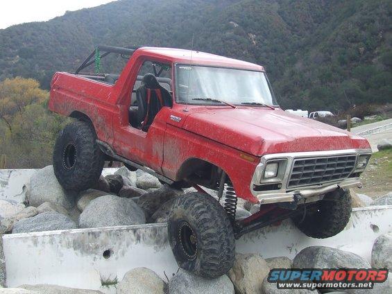 Red 1978 Ford Bronco with off-road tires navigating rocks