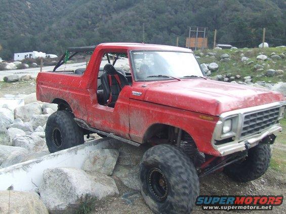 Red Bronco on rocks, lifted with big tires. Roll cage installed