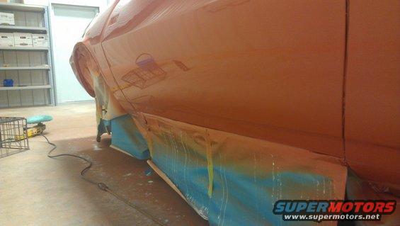 Orange car body side, masked for painting, with reflections of a wire cage