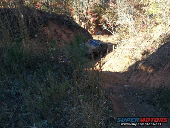 Off-road vehicle on a steep dirt path, with trees and dry grass
