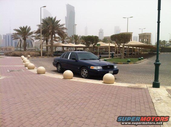Dark blue 2007 Ford Crown Victoria parked on a paved area with concrete spheres, city skyline in background