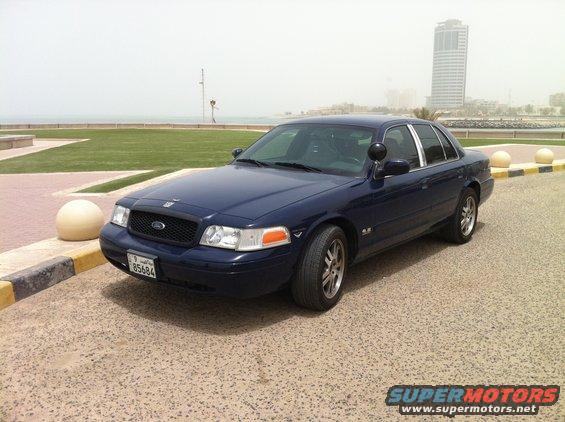 2007 Ford Crown Victoria parked on pavement with a body of water and buildings in the background