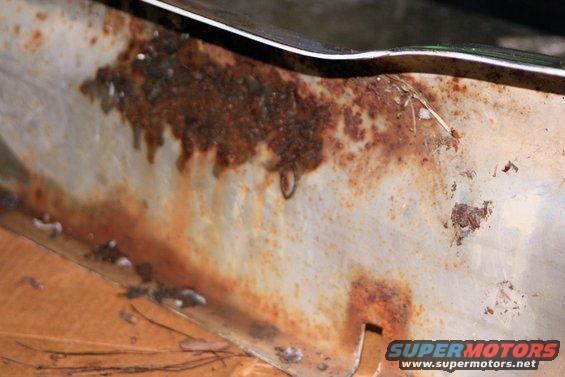 Close-up of a heavily rusted metal panel with a chrome trim piece above
