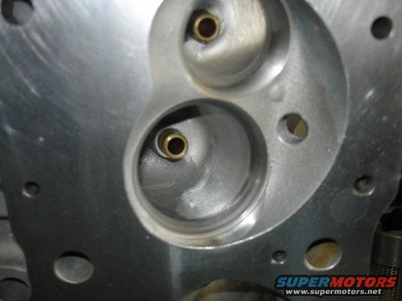 Close-up of an engine cylinder head with two valve openings. One opening has a brass insert