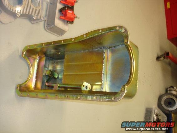 Yellow-coated metal oil pan with visible welds and internal baffles, mounted on a wall