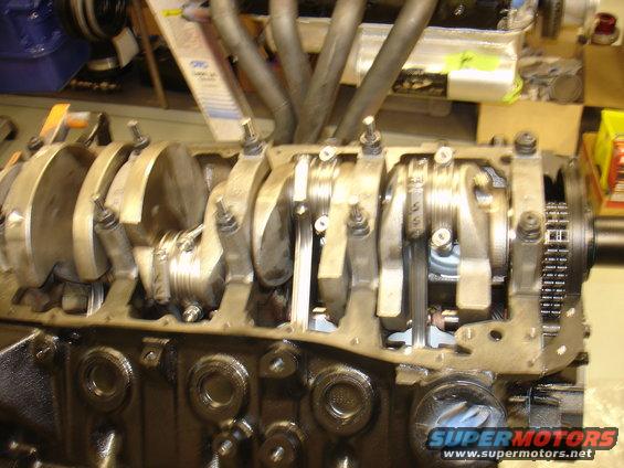 Engine block showing crankshaft, connecting rods, and timing chain. Supermotors.net logo visible