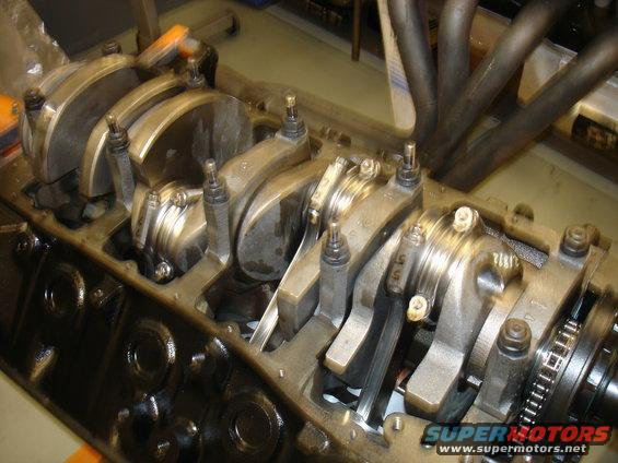 Engine block with crankshaft and connecting rods visible. Exhaust headers are in the background