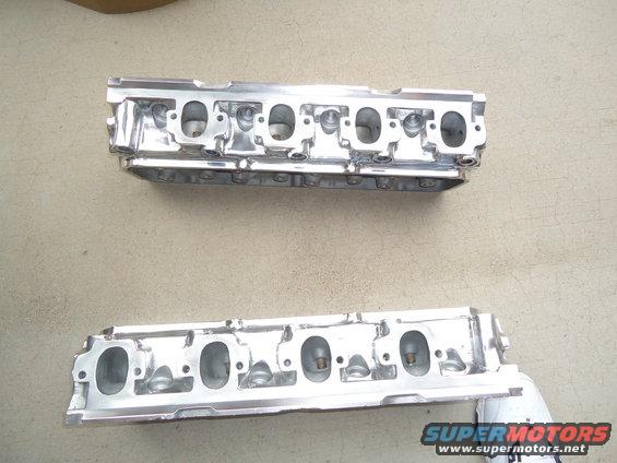 Two polished aluminum engine cylinder heads on a concrete surface