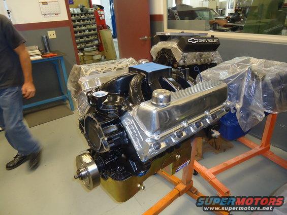 Two Chevrolet V8 engines on orange stands in a workshop. One engine has a black valve cover with a Chevrolet logo