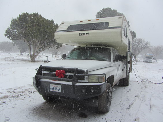 White Dodge 3500 pickup with a Lance camper, parked in snow. License plate 6HKU446