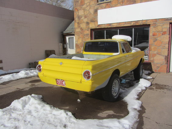 Yellow pickup truck parked outside a building with snow on the ground. License plate reads 7311-NX