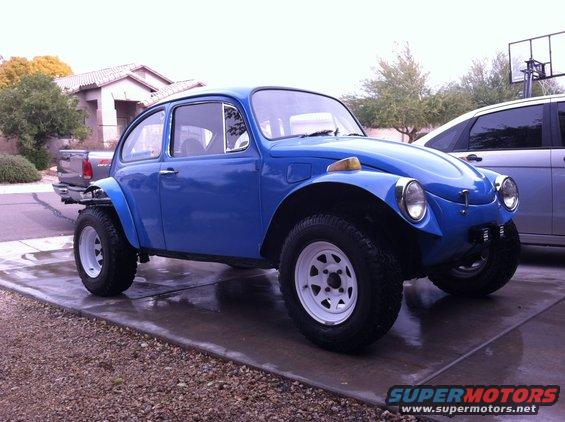 Blue 1970 Volkswagen Beetle Baja Bug with off-road tires and white rims parked on a wet driveway