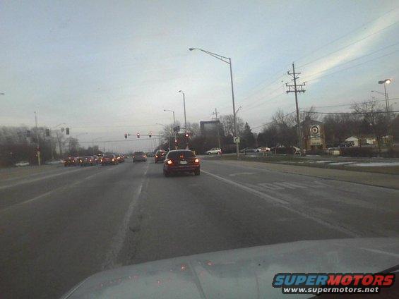Cars driving on a multi-lane road with traffic lights and power lines overhead
