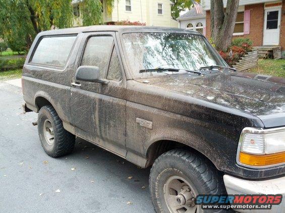 Black Ford Bronco covered in mud, parked on a street