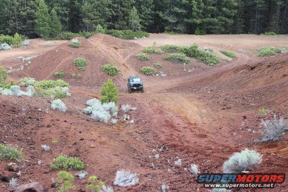 Black SUV driving off-road on a dirt hill with sparse vegetation