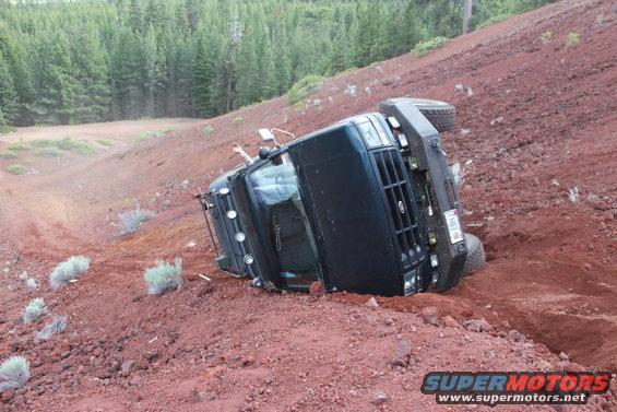 Black 1995 Ford Bronco rolled onto its side on a red dirt slope