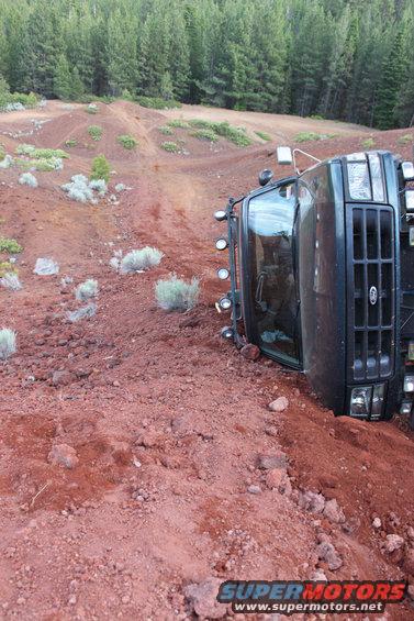 Truck tipped over on a dirt hill with trees in the background
