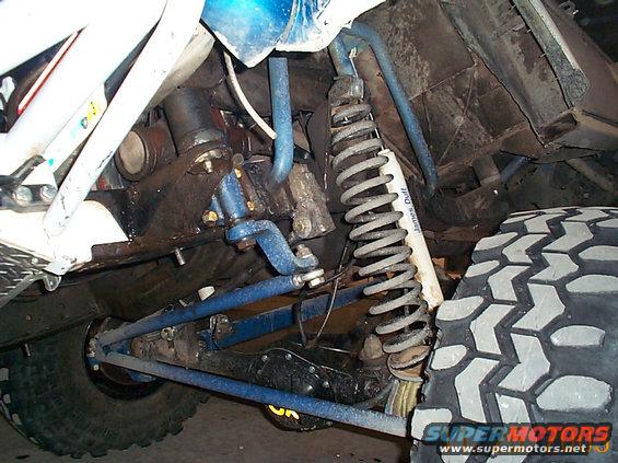 Close-up of off-road vehicle's front suspension with coil spring and shock absorber. Large mud-terrain tire visible