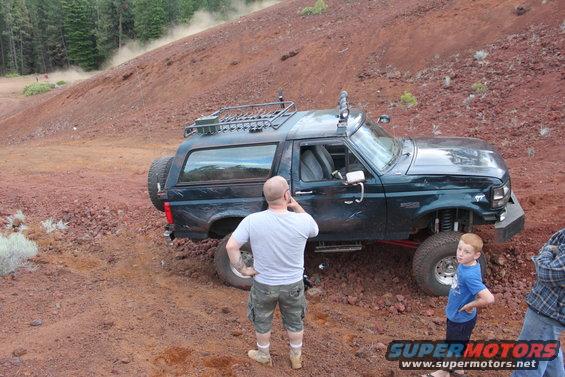 Dark green 1995 Ford Bronco with roof rack and spare tire, off-roading on a dirt hill