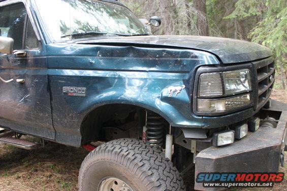 Green Ford Bronco with dented hood and fender. Bronco emblem visible on fender